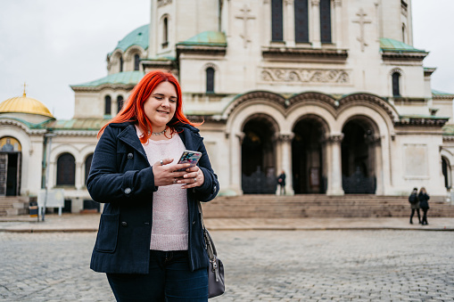 Young plus size woman using her smart phone in front of the St Alexander Nevsky Cathedral In Sofia, Bulgaria.