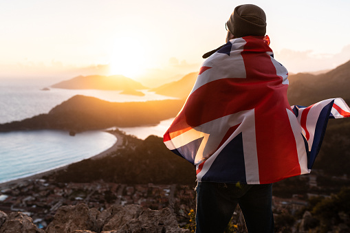 Young woman on the beach at sunset takes a selfie portrait while holding an Australian flag in the air.