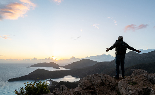 Freedom of travel. Tourist enjoys picturesque look of sea and mountains at sunset, standing on the top.