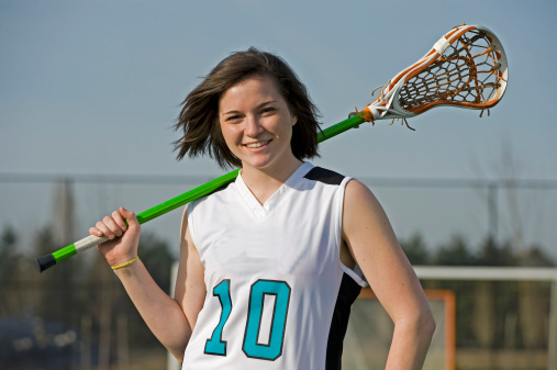 High school girls lacrosse player posing with her stick and the wind blowing in her hair.