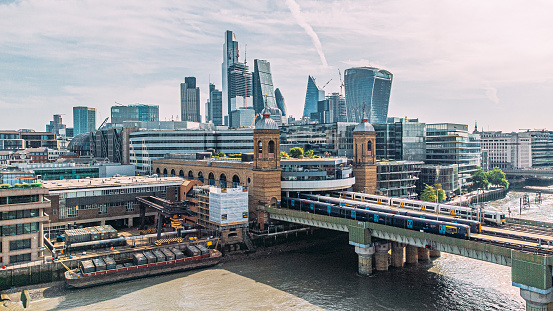 Elevated View of long Passenger Trains Crossing the Cannon Street Railway Bridge crossing the Thames River with the Skyline of London, England in the Background