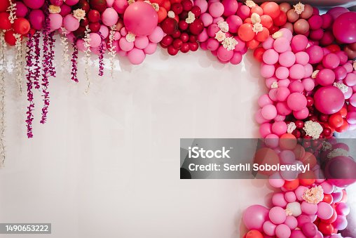 istock Arch with balloons, flowers for party. White photo wall decoration space or place with pink, red, maroon, burgundy balloons. Trendy spring decor. Celebration concept. Birthday party. Wedding reception 1490653222