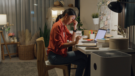 Young Asian woman wear casual sit front of desk with computer laptop feeling unhappy stressed about debt problem on work idea in living room at house at night. Work from home concept.
