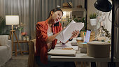 Young Asian woman use mask sheet sit front of desk with computer laptop and using mobile phone talk with colleague meeting work in living room at house at night. Work from home.