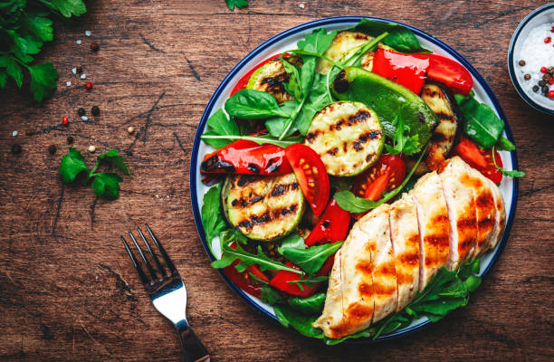 Grilled vegetables and chicken fillet salad with spinach. Paprika, zucchini, eggplant, tomatoes on rustic wooden table background, top view stock photo