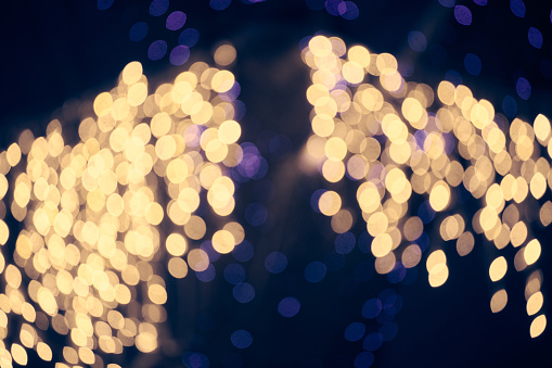 Pale yellow lights bokeh from christmas holiday garlands, blurred festive background, abstract outdoor lights with boke. Yellowish bokeh lights with beautiful shiny on dark night background
