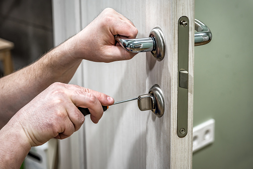Professional handyman repair the door lock in the room, locksmith fixing lock with screwdriver. Industrial theme