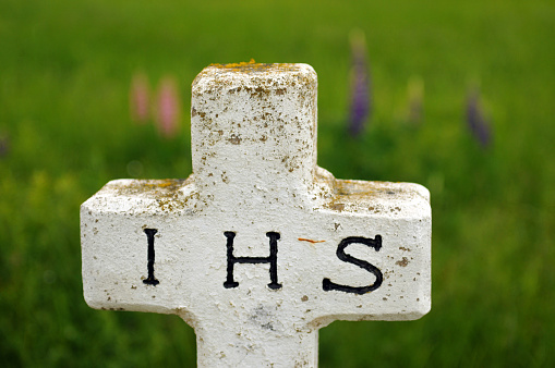 A white stone cross with the letters IHS marks a grave in a Roman Catholic cemetery in Prince Edward Island, Canada.