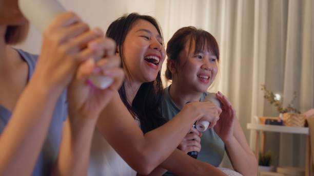 primer plano de jóvenes amigas asiáticas cantando karaoke divirtiéndose en una colorida fiesta en casa por la noche. estilo de vida juntos. - sofa music teenager friendship fotografías e imágenes de stock