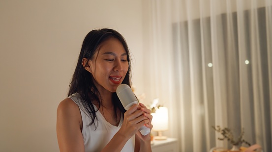 Young Asian female friends singing karaoke having fun at colorful house party at night. Lifestyle together.