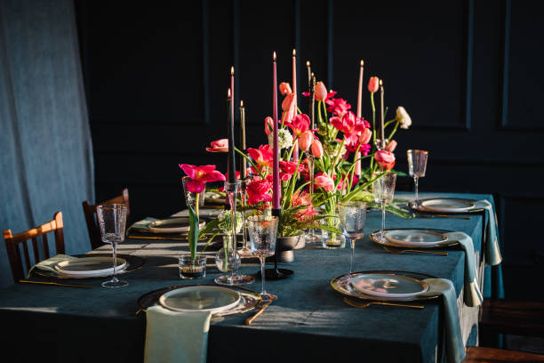 Festive dinner table is served dishes and cutlery and decorated with flowers tulips and greenery, candles. Birthday celebration. Family holidays in modern dining room. Stylish spring party. Wedding.