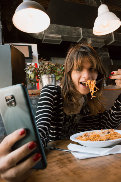 pionowy obraz młodej transpłciowej kobiety jedzącej spaghetti w restauracji i robiącej selfie - contreras zdjęcia i obrazy z banku zdjęć