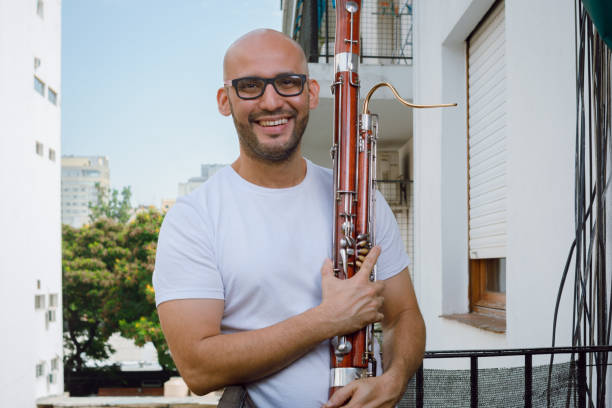 portrait of a young latin man musician saxophonist holding a bassoon on the balcony of his apartment - bassoon imagens e fotografias de stock