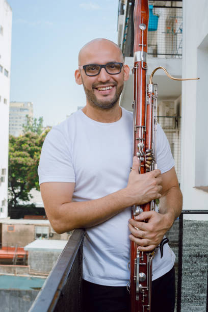 young latino venezuelan man standing on a balcony holding a bassoon, waist up vertical portrait stock photo