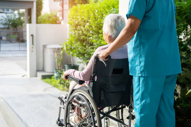 caregiver help and care asian senior or elderly old lady woman patient sitting on wheelchair to ramp in nursing hospital, healthy strong medical concept. - ouderenzorg stockfoto's en -beelden