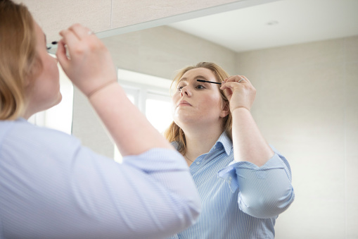Young woman putting the finishing touches to her make-up in front of a domestic bathroom mirror