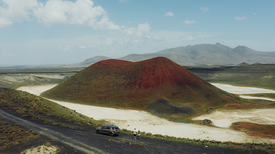 Drone high-angle photo of a couple enjoying a journey to the mountains, contemplating the green volcanic landscape with a bright red crater of the volcano surrounded by the salt Meke lake, Turkey