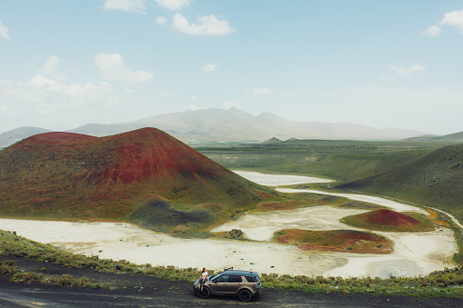 Drone high-angle photo of female enjoying a journey to the mountains, contemplating the green volcanic landscape with a bright red crater of the volcano surrounded by the salt Meke lake, Turkey
