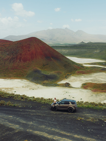 Drone high-angle photo of female enjoying a journey to the mountains, contemplating the green volcanic landscape with a bright red crater of the volcano surrounded by the salt Meke lake, Turkey