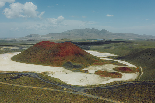 Drone high-angle photo of a couple enjoying a journey to the mountains, contemplating the green volcanic landscape with a bright red crater of the volcano surrounded by the salt Meke lake, Turkey