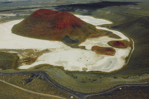 Drone high-angle photo of a couple enjoying a journey to the mountains, contemplating the green volcanic landscape with a bright red crater of the volcano surrounded by the salt Meke lake, Turkey