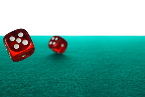 Two red dices rolling over a green felt against a white background.