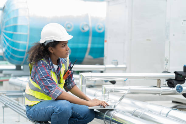 ingénieure utilisant un ordinateur portable inspectant des tuyaux d’égout de qualité sur le toit du bâtiment. ingénieure afro-américaine travaillant, vérifiant ou entretenant des conduites d’égout sur un chantier de construction - working plumber water pipe repairing photos et images de collection