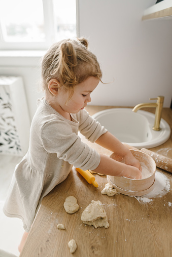 Child knead dough, cooks pizza, bake cookies, dumplings, croissants for mother, father. Little kid daughter having fun cooking pastries or pie on kitchen table top. Family preparation food on weekend.