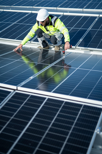 Male technician on a roof repairing solar panels.