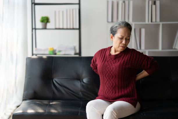istock Senior woman having back pain, rubbing her back while sitting on the sofa, feeling upset and in pain. 1490668596