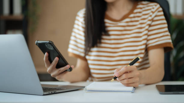 istock Woman hand working at a smartphone, computer and writing on a notepad with a pen in the home office. 1490668742
