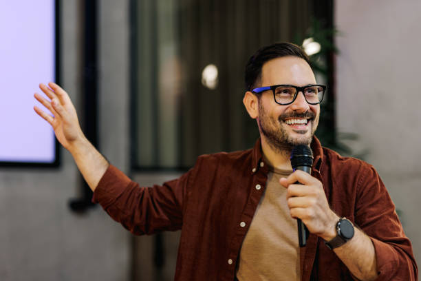 istock Happy man giving a speech, holding a microphone, pointing on a projection screen. 1490670967