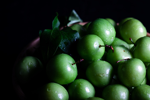Close-up of fresh green plums in a bowl on dark background. Green plum fruit.