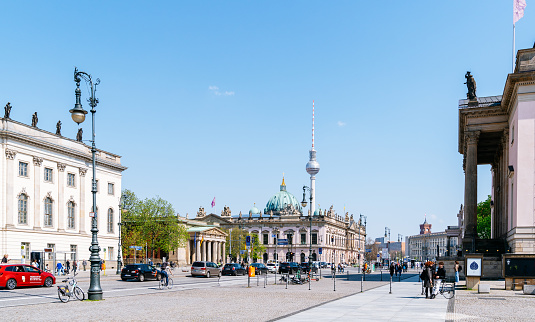 The photo captures Berlin's city center on a sunny day, with the iconic Fernsehturm and Berliner Dom in the background. The road is busy with cars, capturing the bustling energy of the city.