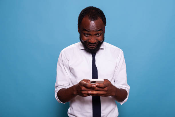 istock Man in white shirt holding smartphone playing mobile game looking excited at screen 1490674770