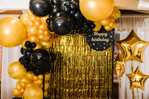 Arch decorated with black, brown, golden balloons and stars. Photo-wall decoration space, place with gold background. Trendy autumn decor. Celebration concept. Birthday party. Happy birthday text.