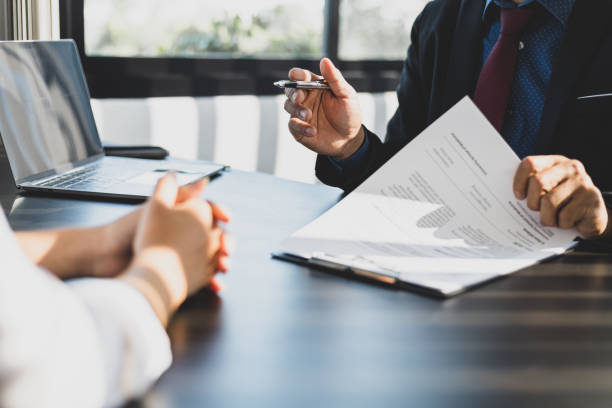 empresário de terno em seu escritório mostrando uma apólice de seguro e apontando com uma caneta onde o segurado deve assinar. apresentação do agente de seguros e consultoria de detalhes do seguro ao cliente. - sistema legal - fotografias e filmes do acervo