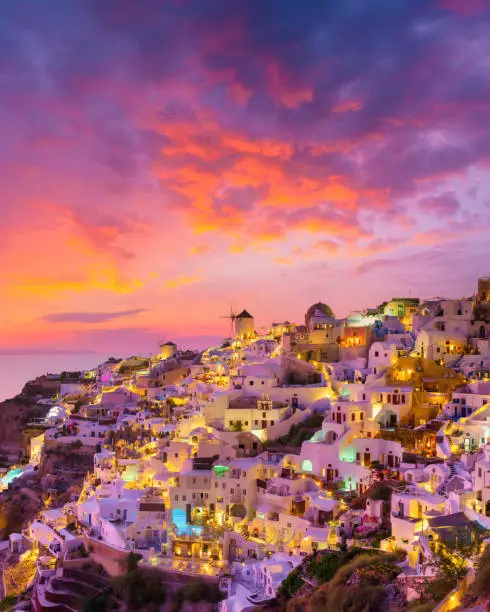 Photo of Oia village, Santorini, Greece. Vacation. View of traditional houses in Santorini. Small narrow streets and rooftops of houses, churches and hotels. Landscape during sunset.