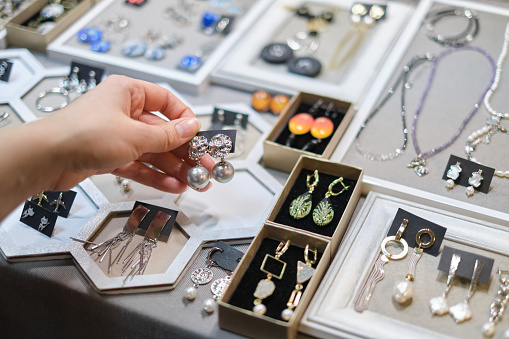 beautifully crafted earring is being chosen by a woman's hand, with a diverse selection of handmade bijouterie adorning the stall behind. art of creating handmade jewelry,
