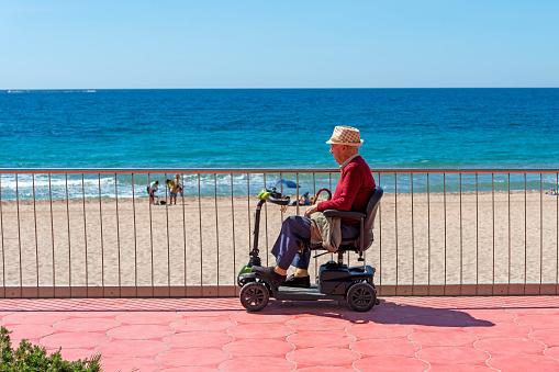 benidorm spain april - 15 - 2023 - unknown alone man sits in  one motorized chair and looking out over the sea in the city of benidorm in spain in spain in alicante province