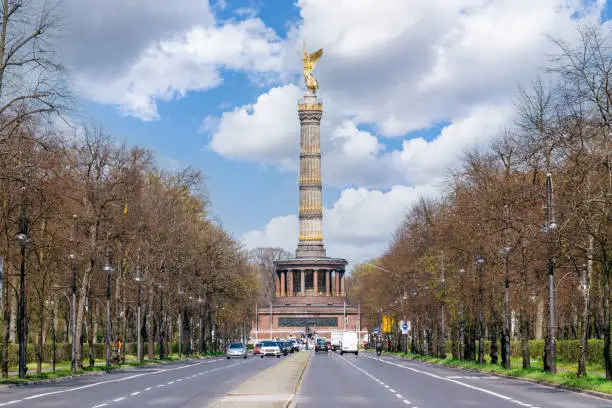 A sunny spring day in the Tiergarten park in the Mitte district of Berlin, Germany. The 17th June Street is in the foreground, and the Victory Column is in the background. The sky is blue with fluffy clouds.