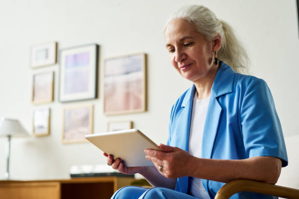 istock Smiling mature female broker or analyst in blue smart casualwear using tablet 1490676367