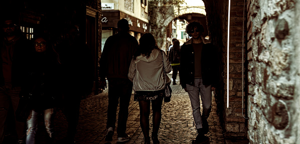 Sirmione, Italy 11 april 2023: Group of people leisurely walking through the dark arches of a historical city's portico