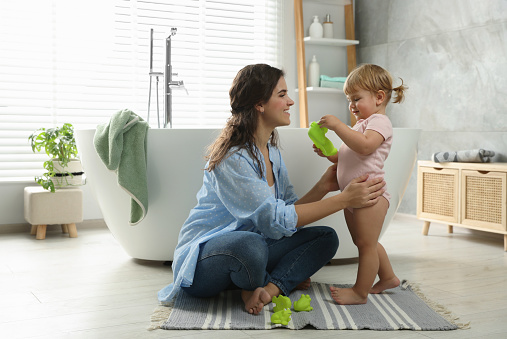 Mother playing with her daughter near tub in bathroom