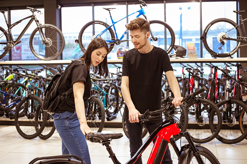 Salesman and young woman watching electric bicycle in bike shop. Young man selling bikes.