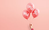 Hand of woman holding pink balloons with percent on pink background, Minimal, Sale and discount. copy space.