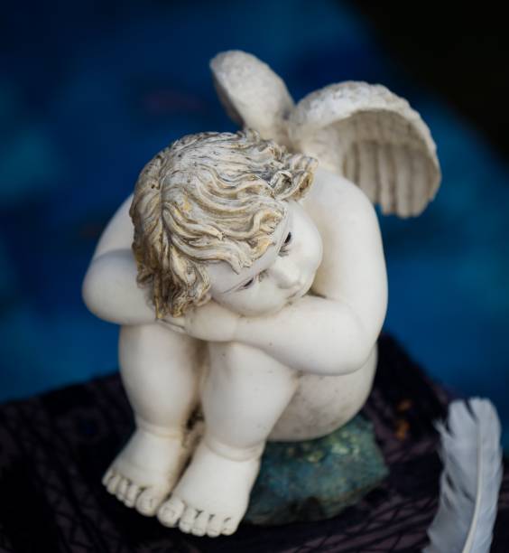 istock Small angel figurine with white wings and feathers is seated in a relaxed pose 1490686313