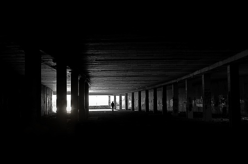 A silhouette of a man in the tunnel with a series of stone pillars illuminated in the darkness.