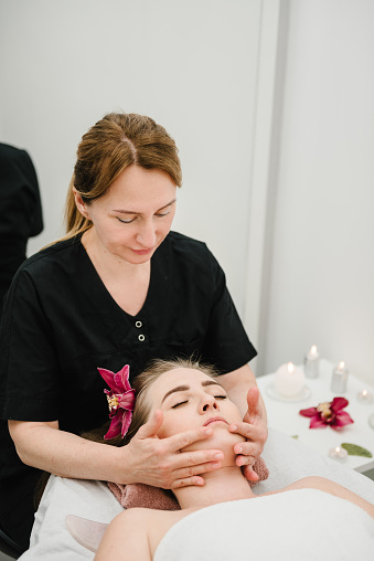 Cosmetologist making rejuvenating face procedures client in spa salon. Aesthetic cosmetology, face care. Facial treatment, skincare concept. Girl getting face, head massage treatment. Relaxing massage