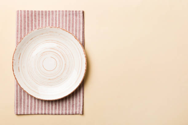 istock Top view on colored background empty round white plate on tablecloth for food. Empty dish on napkin with space for your design 1490694323